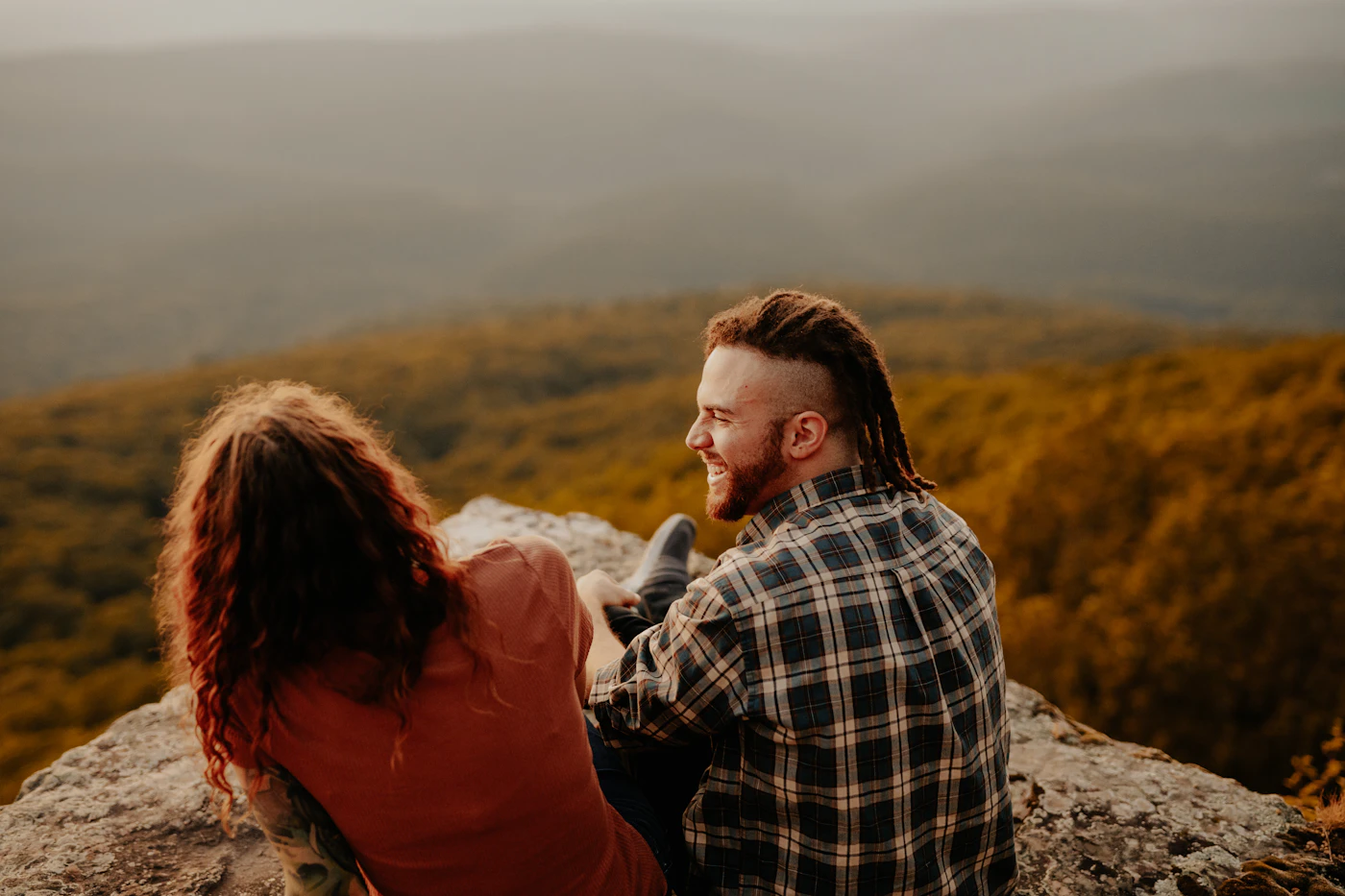 Nora and Jalen sitting close on a rock, looking out over misty mountain ridges