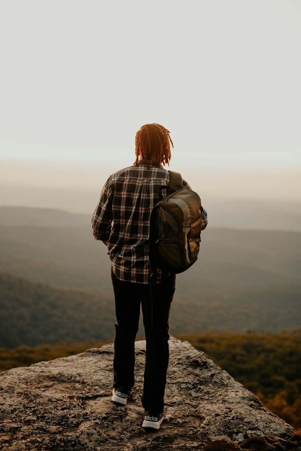 woman in brown and white plaid dress shirt and black pants standing on rock during daytime