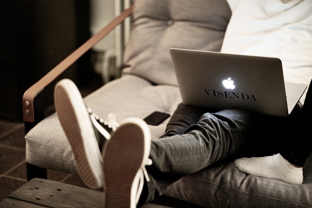 man in white long sleeve shirt and blue denim jeans sitting on brown sofa using macbook
