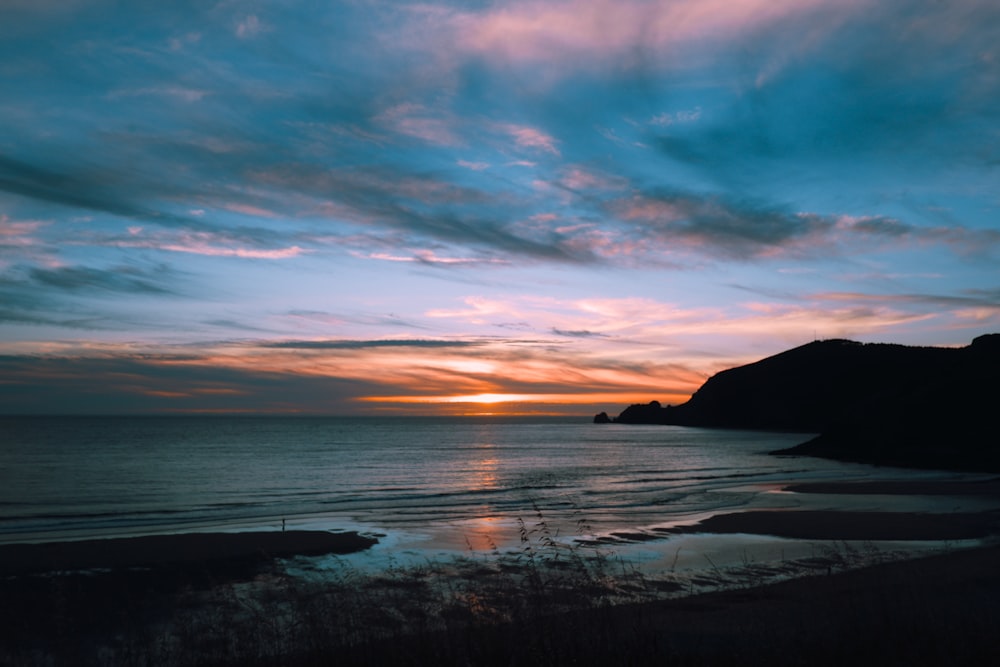 silhouette of mountain near body of water during sunset