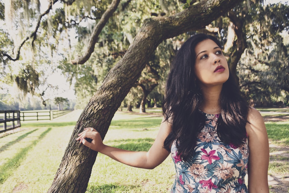 woman in black red and white floral sleeveless dress standing beside brown tree during daytime