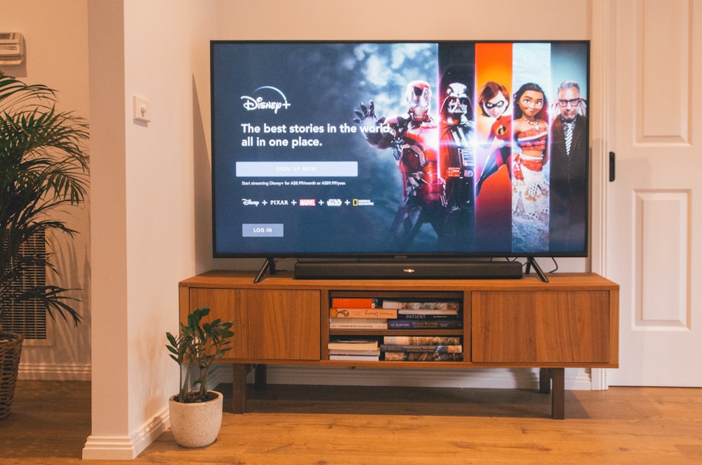 Televisor de pantalla plana negro encendido en estante de TV de madera marrón