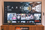 A television screen displaying the Netflix interface is shown. The main focus is the show 'Dark' with a large image from the series. Below it are recommendations for 'Continue Watching,' including shows like 'Selling Sunset,' 'Friends,' and 'Community.' The interface includes the Netflix logo and an array of show thumbnails.
