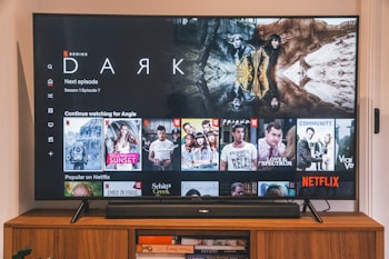 A television screen displaying the Netflix interface is shown. The main focus is the show 'Dark' with a large image from the series. Below it are recommendations for 'Continue Watching,' including shows like 'Selling Sunset,' 'Friends,' and 'Community.' The interface includes the Netflix logo and an array of show thumbnails.
