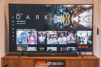 A television screen displaying the Netflix interface is shown. The main focus is the show 'Dark' with a large image from the series. Below it are recommendations for 'Continue Watching,' including shows like 'Selling Sunset,' 'Friends,' and 'Community.' The interface includes the Netflix logo and an array of show thumbnails.