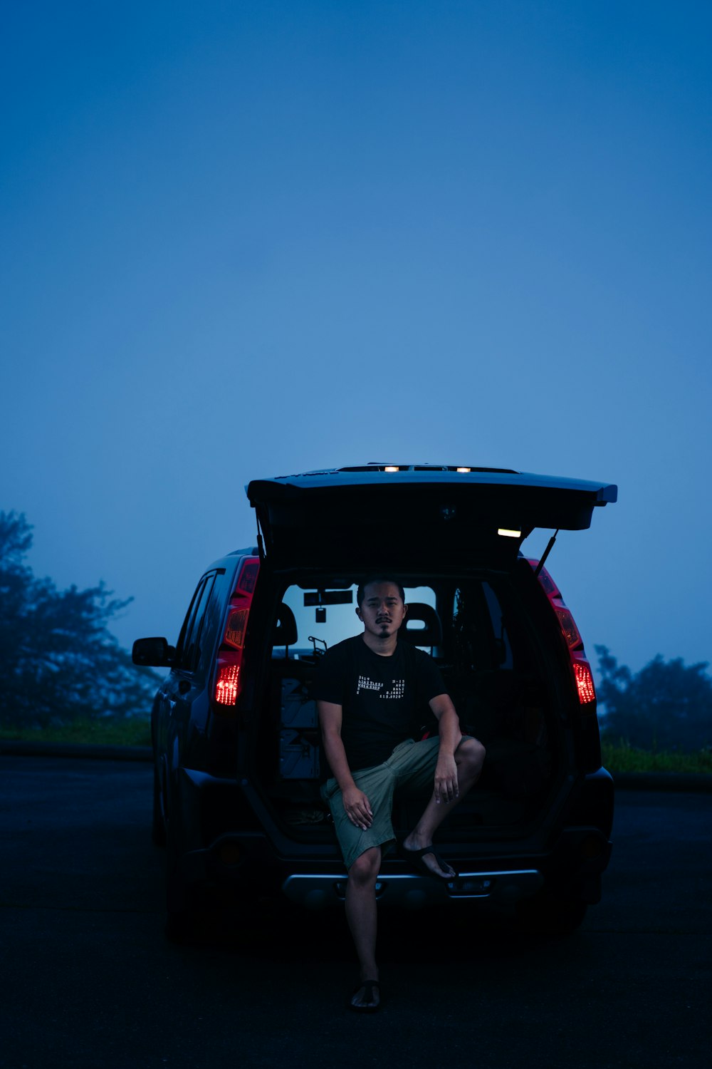 man in black crew neck t-shirt and gray shorts sitting on black suv