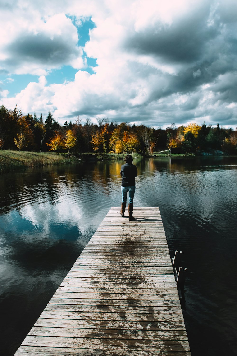 man in black jacket and blue denim jeans standing on dock during daytime