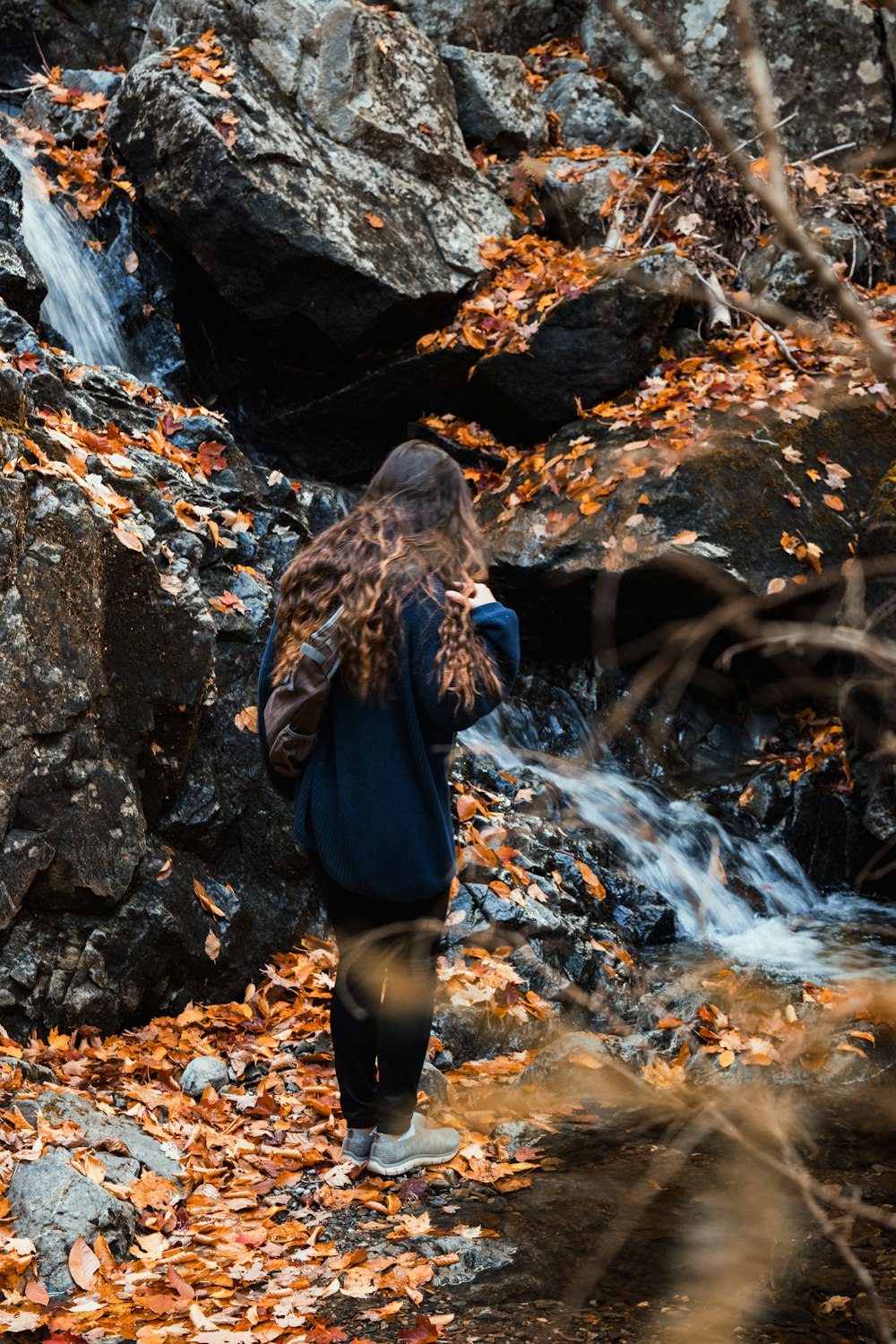 woman in black jacket and black pants standing on rocky river during daytime