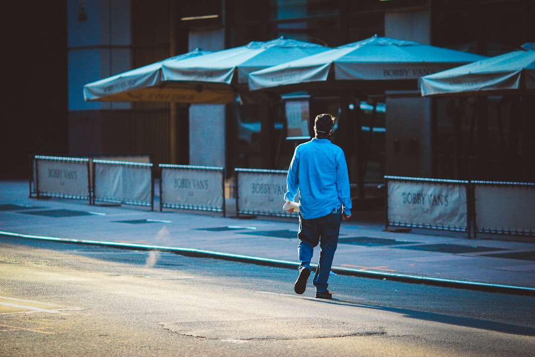 man in white hoodie and black pants walking on sidewalk during daytime