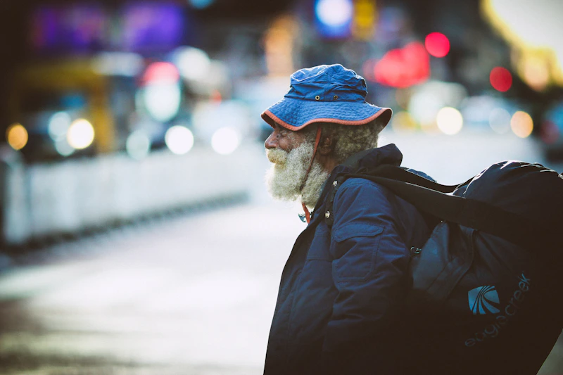 man standing on road in black jacket and blue beanie