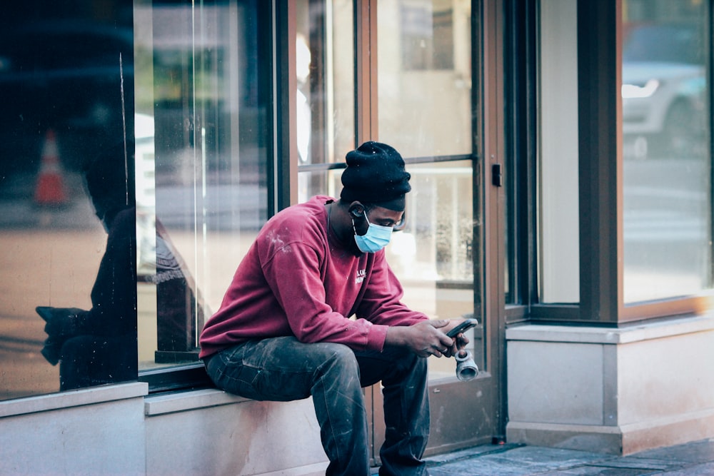 man in red dress shirt and blue denim jeans sitting on window