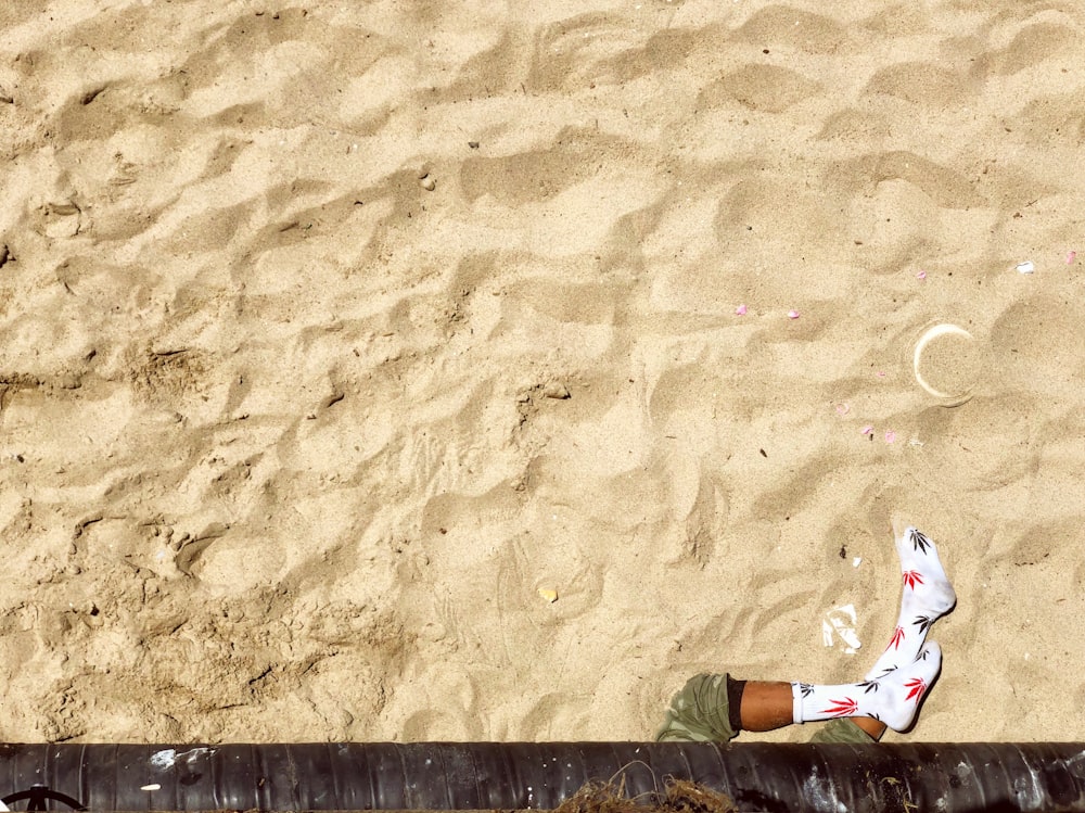 person in black pants and white red and blue floral sneakers standing on brown sand during