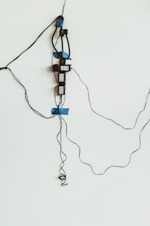 An electrical setup with several electronic devices and wires taped to a white wall. Blue tape is used to secure black cables and devices, which appear to be power adapters or similar equipment.