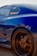 A blue sports car with custom wheels and a visible 'Haltech' sticker on the window. The car is parked on a gravel surface and appears to be in the early evening light, creating a warm glow on the rims.