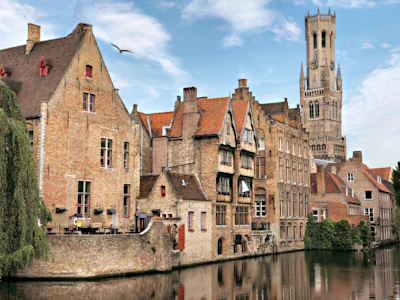 Stepped brick gables reflected in a Bruges canal, with the belfry behind