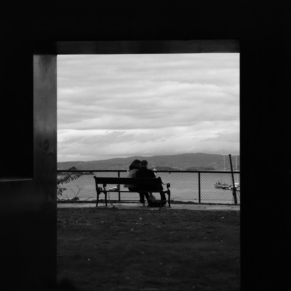 grayscale photo of 2 person sitting on bench