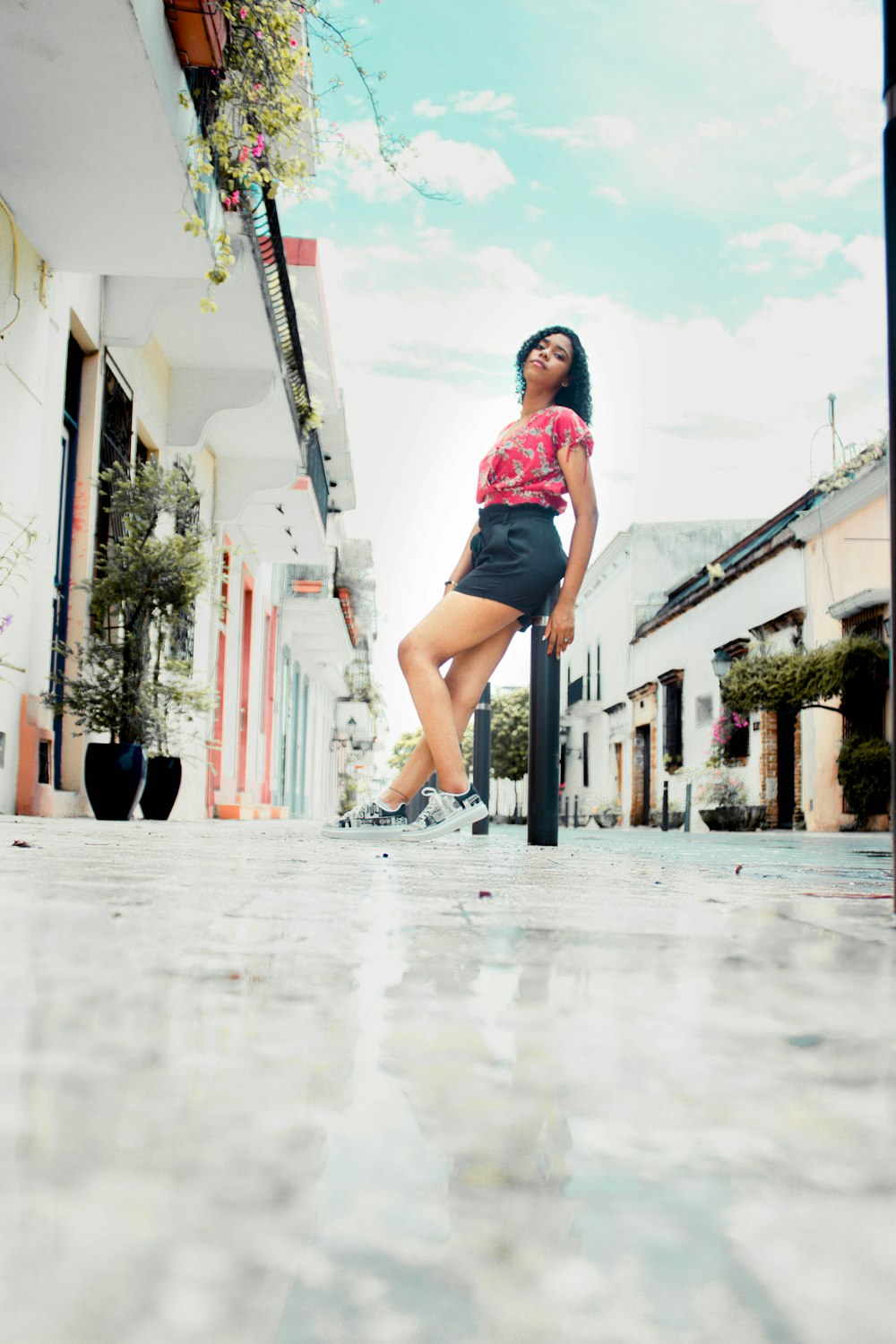 woman in pink shirt and black shorts standing on sidewalk during daytime