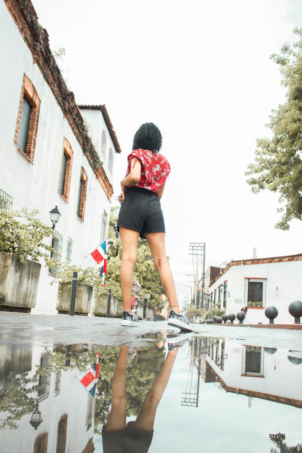 woman in red shirt and black shorts standing on water fountain