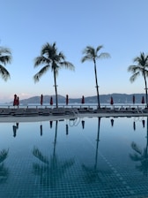 A serene image of a luxury hotel poolside with palm trees under a clear blue sky