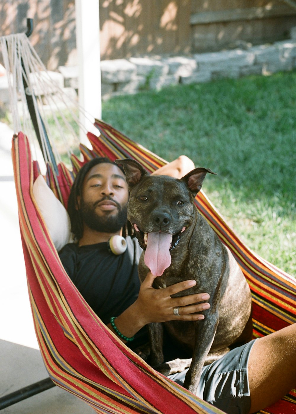 girl in blue dress hugging black short coated dog on hammock during daytime