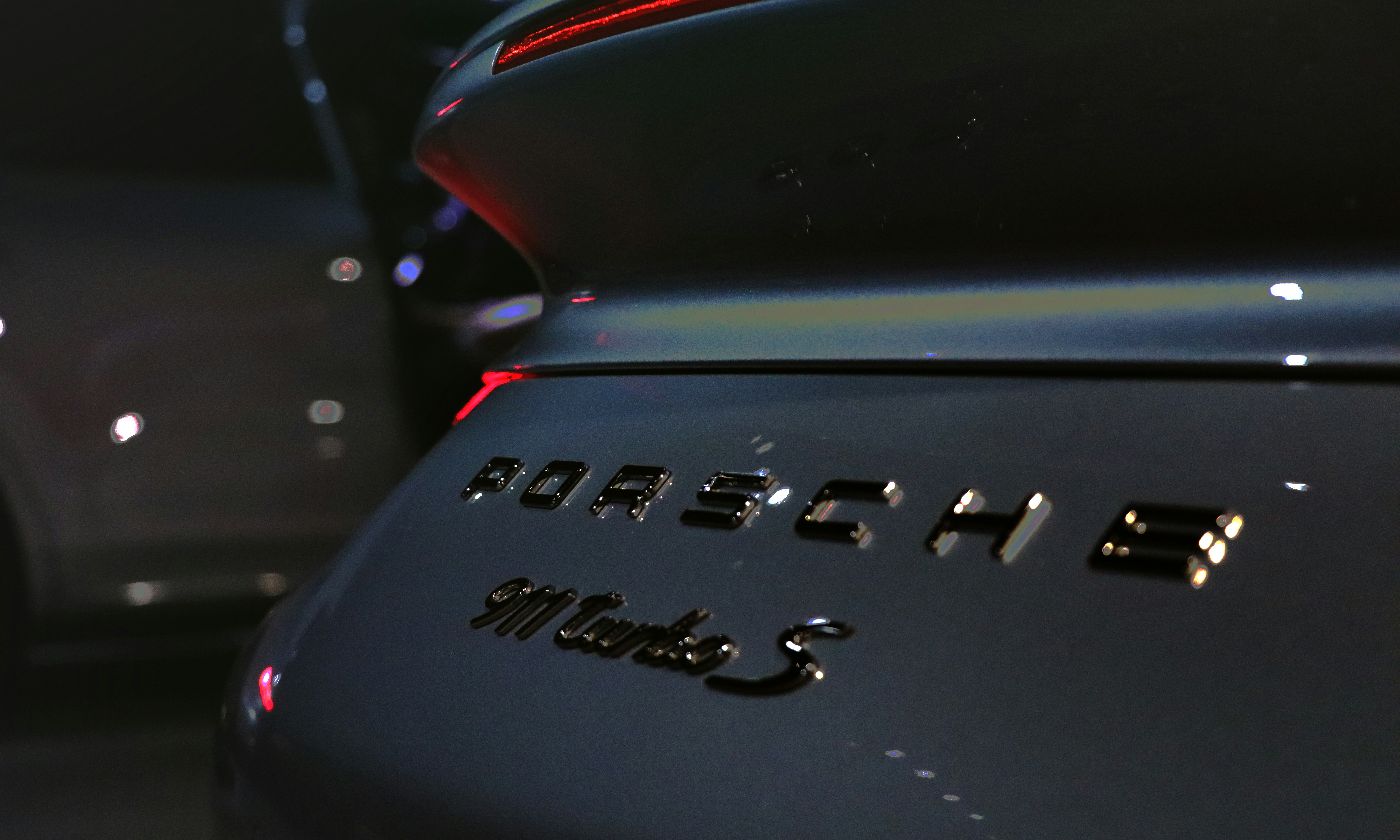 Porsche 911 Turbo S in Guards Red, dark background with dramatic rim lighting highlighting iconic silhouette
