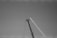 A black and white image of a crane arm extending upward into the sky, with a clear view of the metal structure and cables against a plain background.