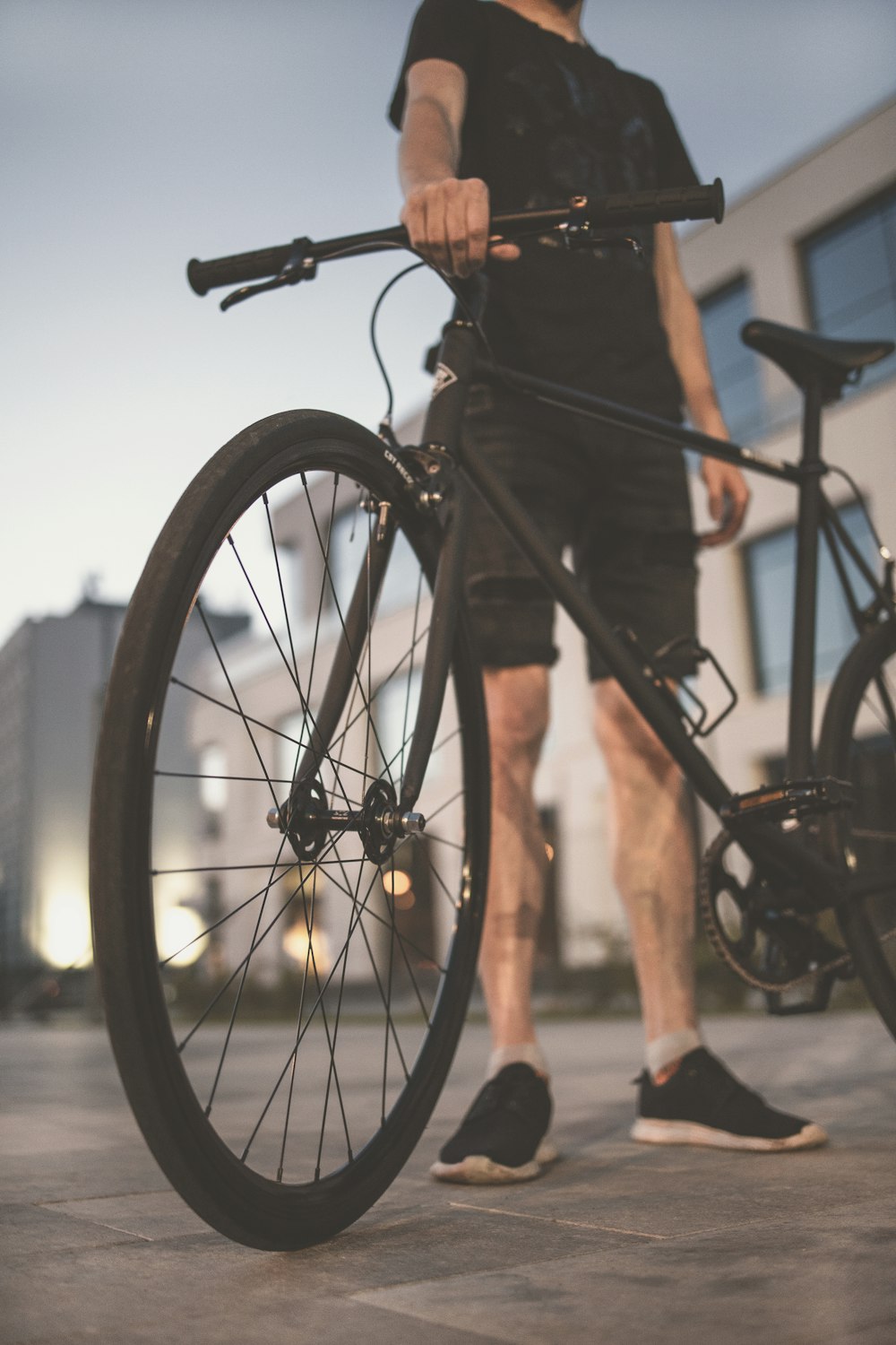 man in black shorts and black shirt standing beside black bicycle during daytime