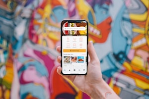 A hand holding a smartphone displaying a user interface for a food delivery app with options for dishes, collections, menus, and places near the user. The background showcases a vibrant and colorful graffiti mural with abstract and humanoid shapes.