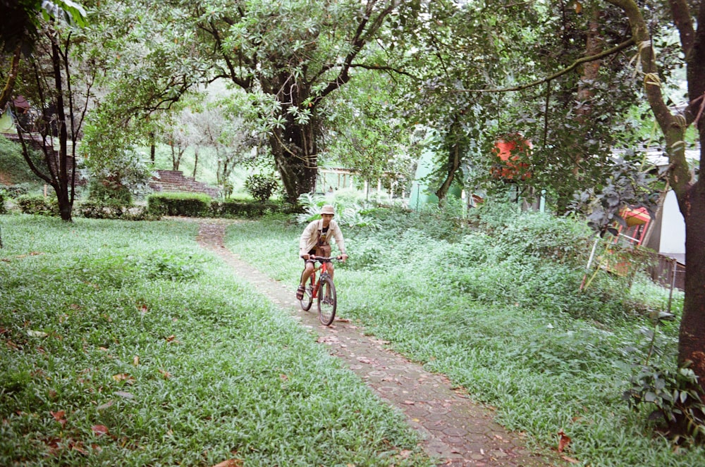 man riding bicycle on pathway between green grass and trees during daytime