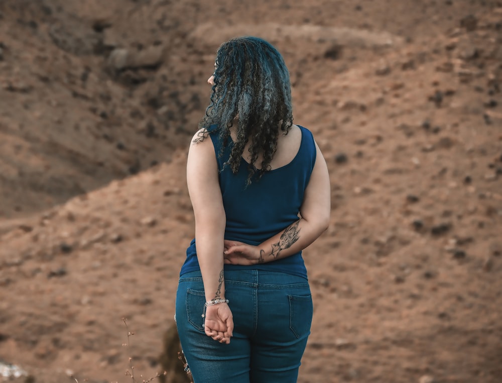 woman in black tank top and blue denim jeans sitting on brown rock during daytime