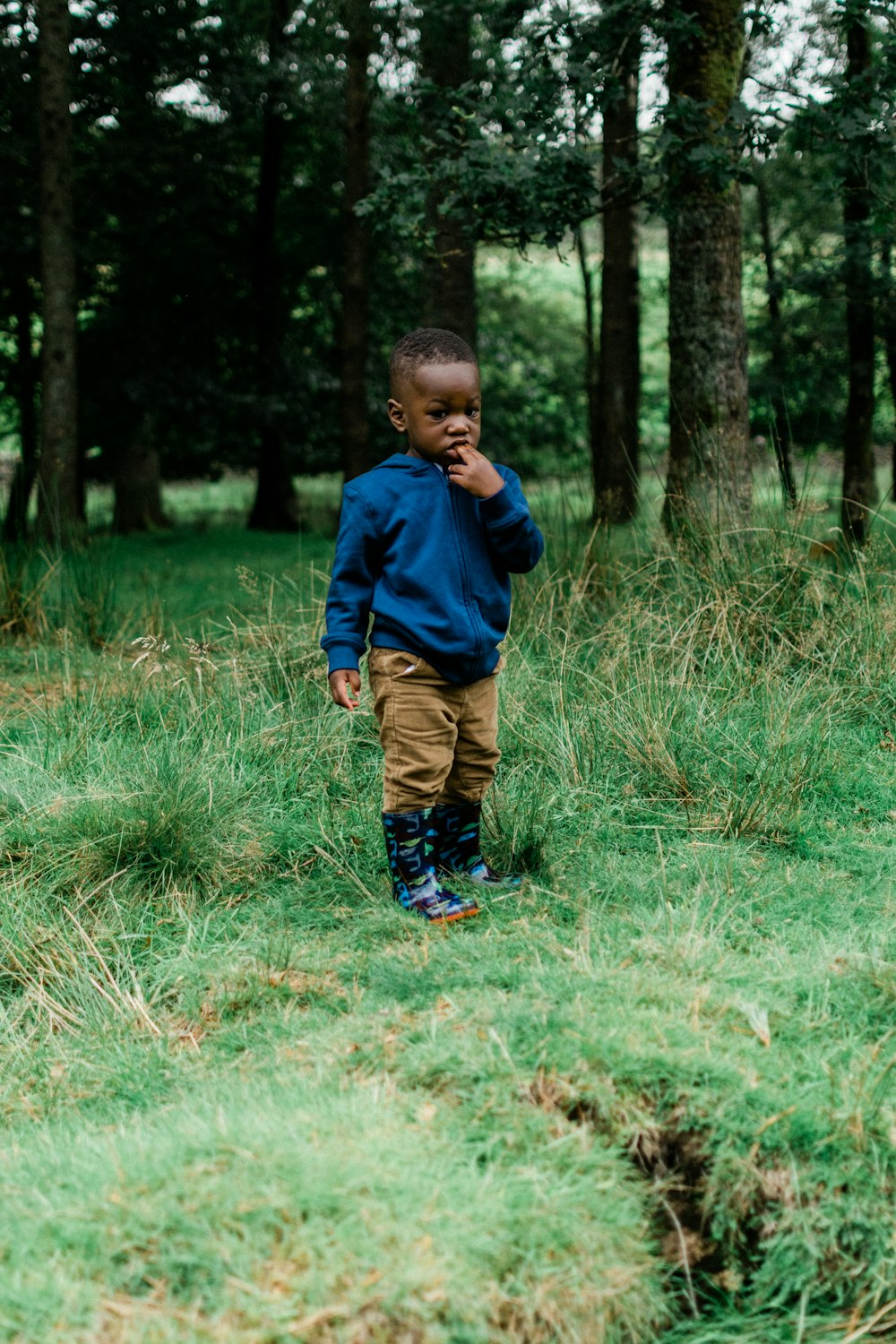 Junge in blauer Jacke geht tagsüber auf grünem Rasen spazieren
