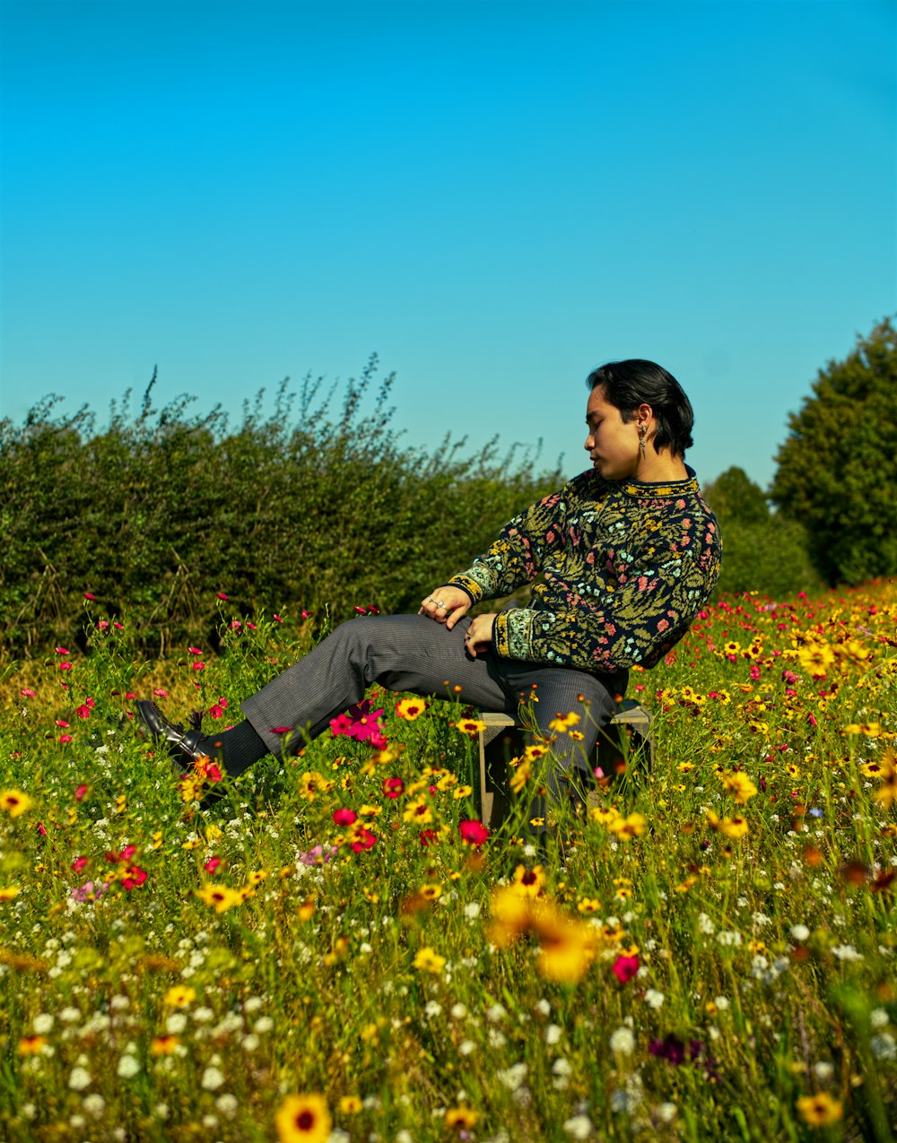man in black and white floral long sleeve shirt sitting on yellow flower field during daytime
