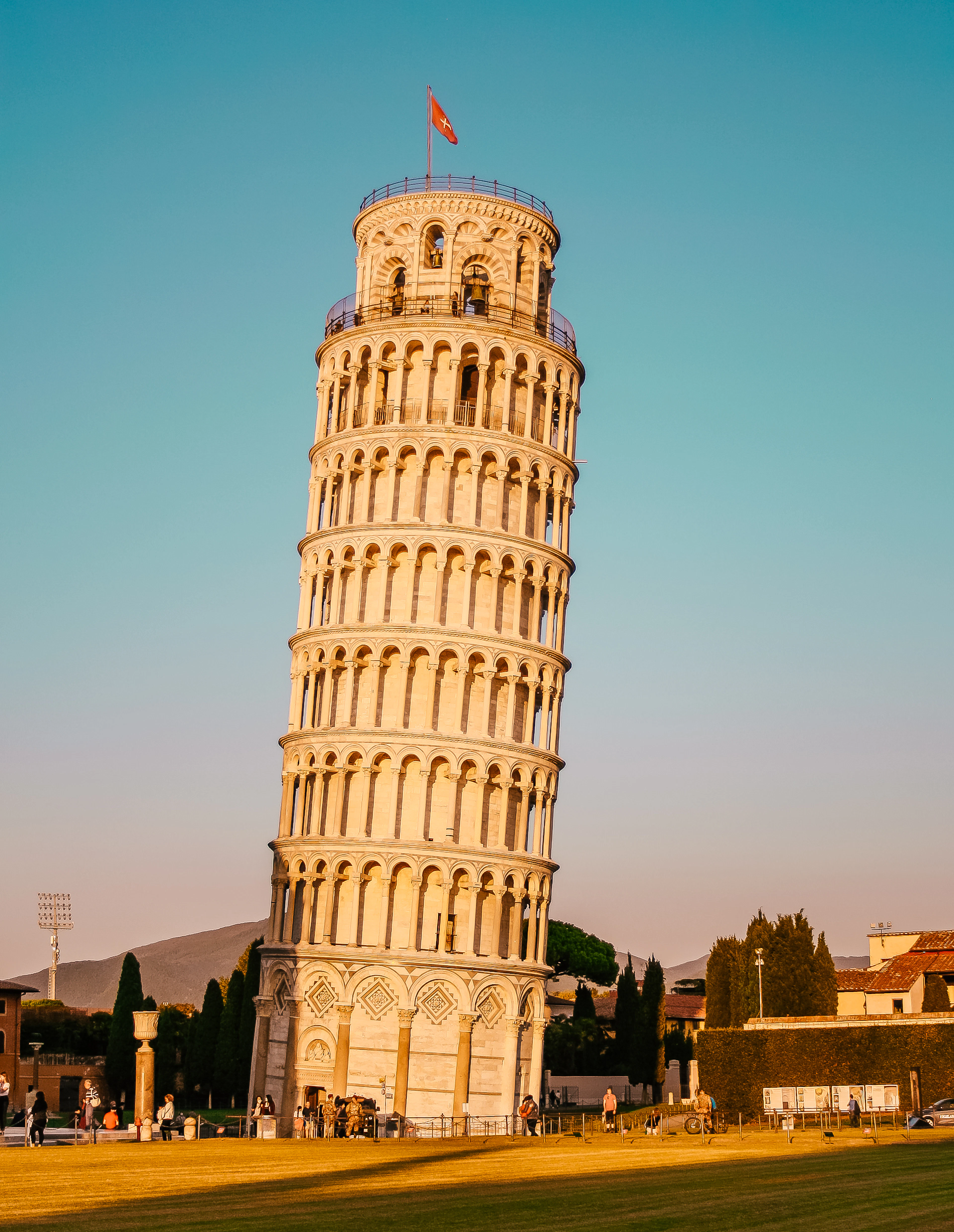 The Leaning Tower of Pisa glowing gold at sunset against a clear blue sky, seen from the ground.