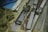 Several metal film splicing tools are arranged on a surface alongside film strips, tangled twine, a metal ruler, and stacks of paper. The scene conveys a vintage or workshop setting, indicative of old-fashioned film editing processes.