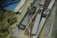Several metal film splicing tools are arranged on a surface alongside film strips, tangled twine, a metal ruler, and stacks of paper. The scene conveys a vintage or workshop setting, indicative of old-fashioned film editing processes.