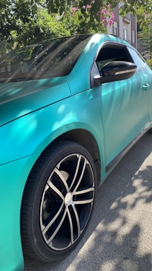 A sleek turquoise car parked near a bustling local market with tropical fruits and flowers.