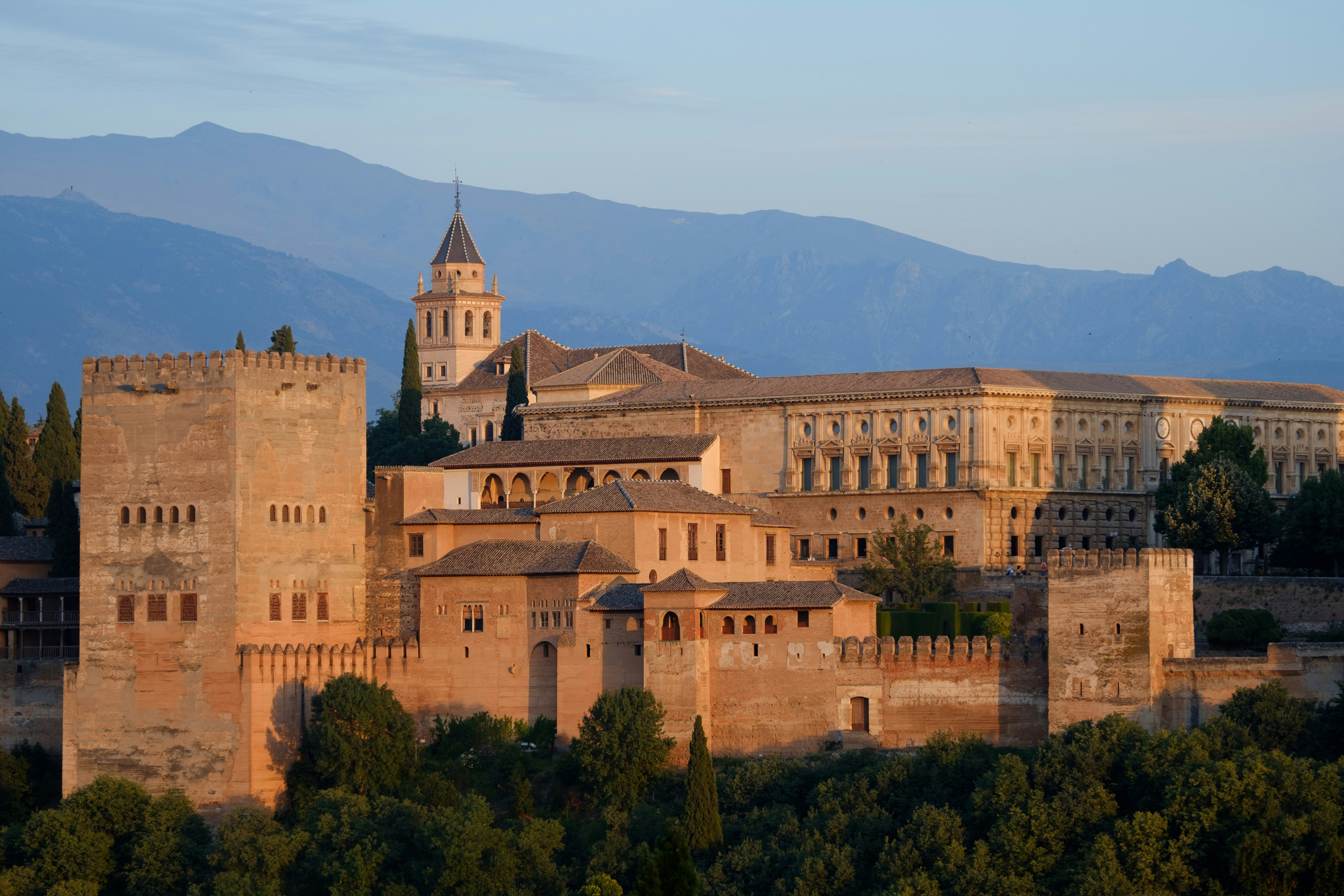 A panoramic view of the Alhambra palace in Granada, Spain, with mountains in the background.