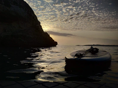 A stand-up paddle board resting on calm blue water with a sunset horizon.