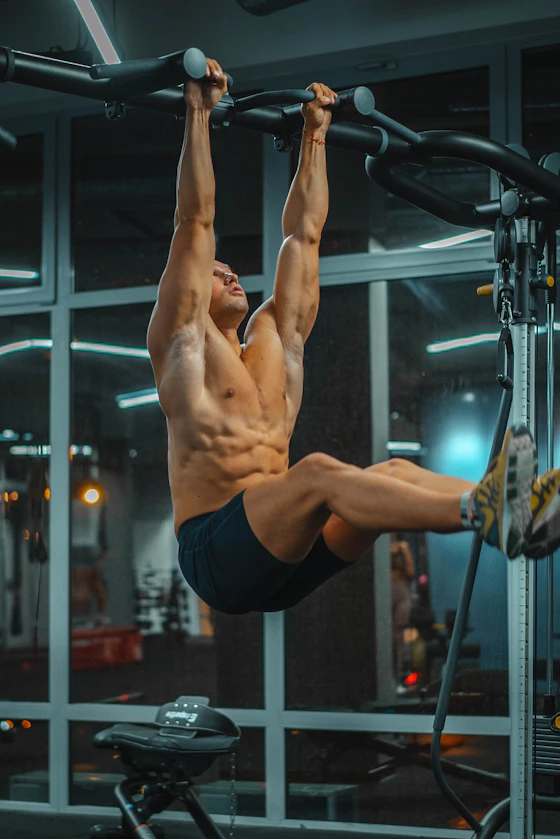 Atleta em elevação de pernas com abdômen definido, luz de academia