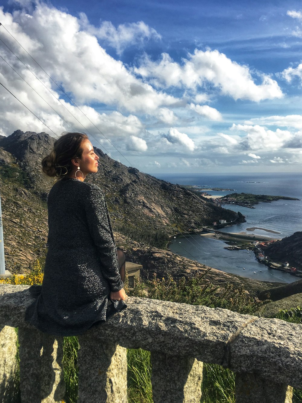 woman in black long sleeve shirt sitting on rock near body of water during daytime