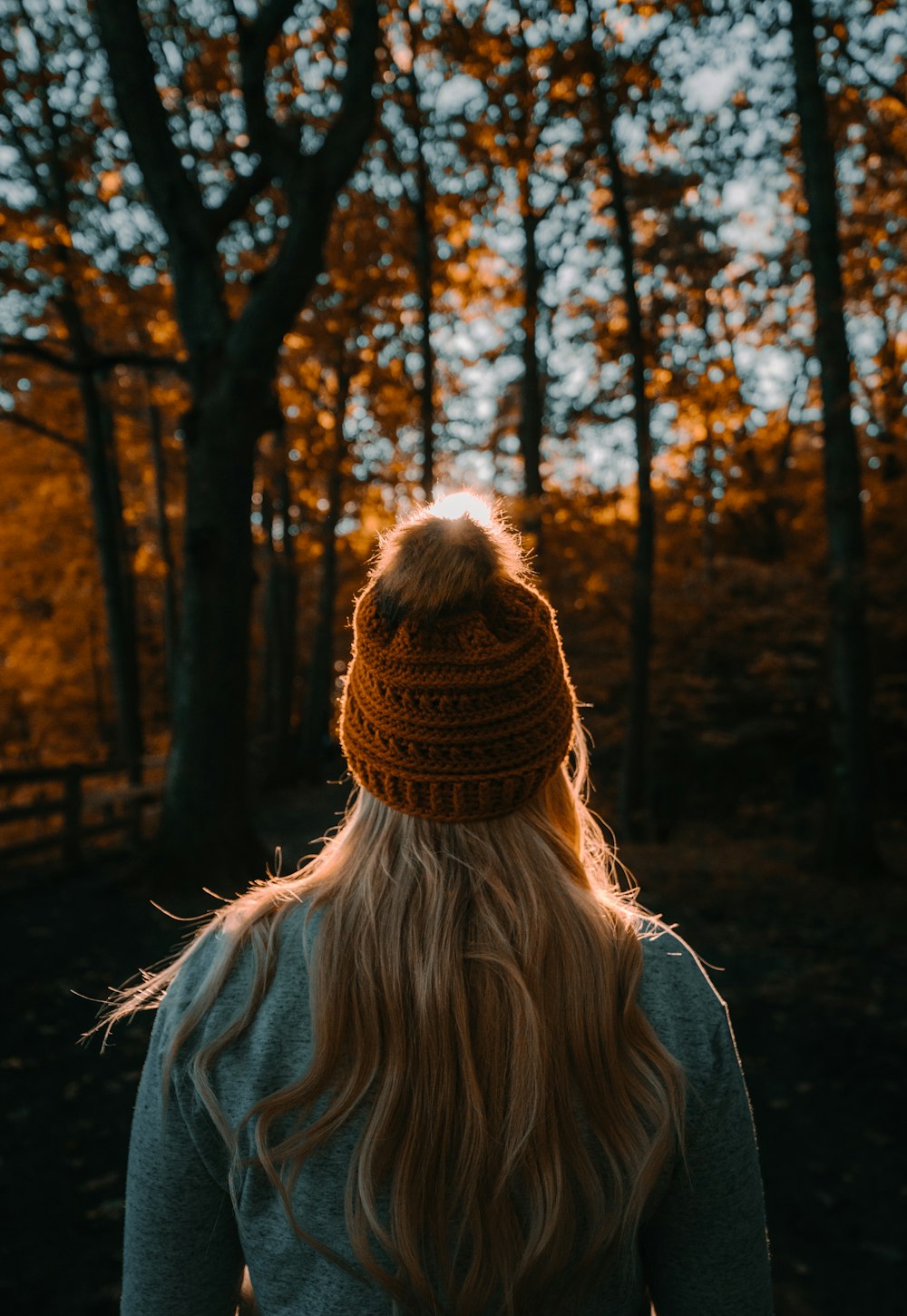 woman in brown knit cap and gray jacket standing in front of brown trees during daytime