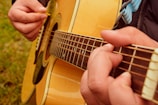 Close-up of hands playing a classic acoustic guitar with a field of corn in the background.
