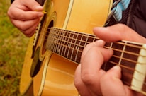 Close-up of hands playing an acoustic guitar with sheet music in the background.