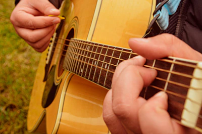 Close-up of hands strumming an acoustic guitar against a beige backdrop.