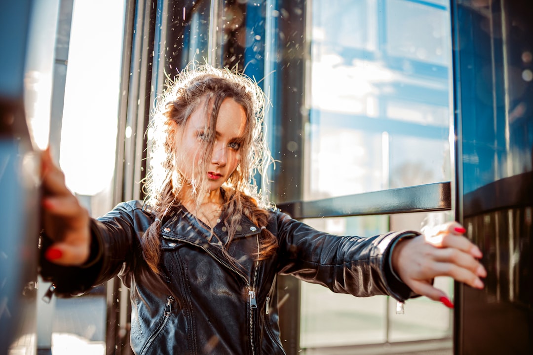 woman in black leather jacket standing near glass window during daytime