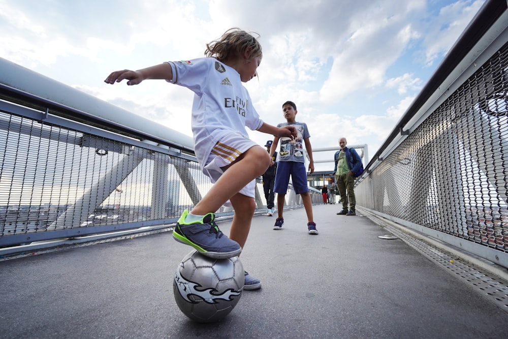 白いTシャツと青い短パンを着た男の子が昼間にサッカーをしている