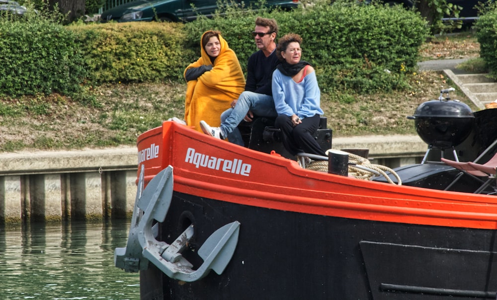 3 men in red and black boat on river during daytime