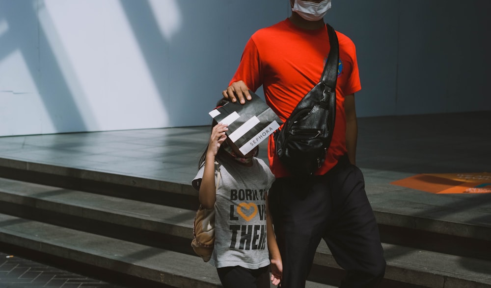 man in red crew neck t-shirt and black pants holding white and black labeled pack