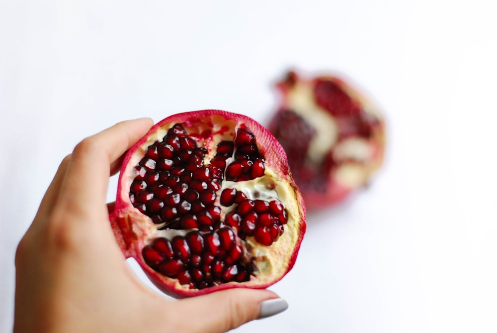 person holding pomegranate fruit on white table