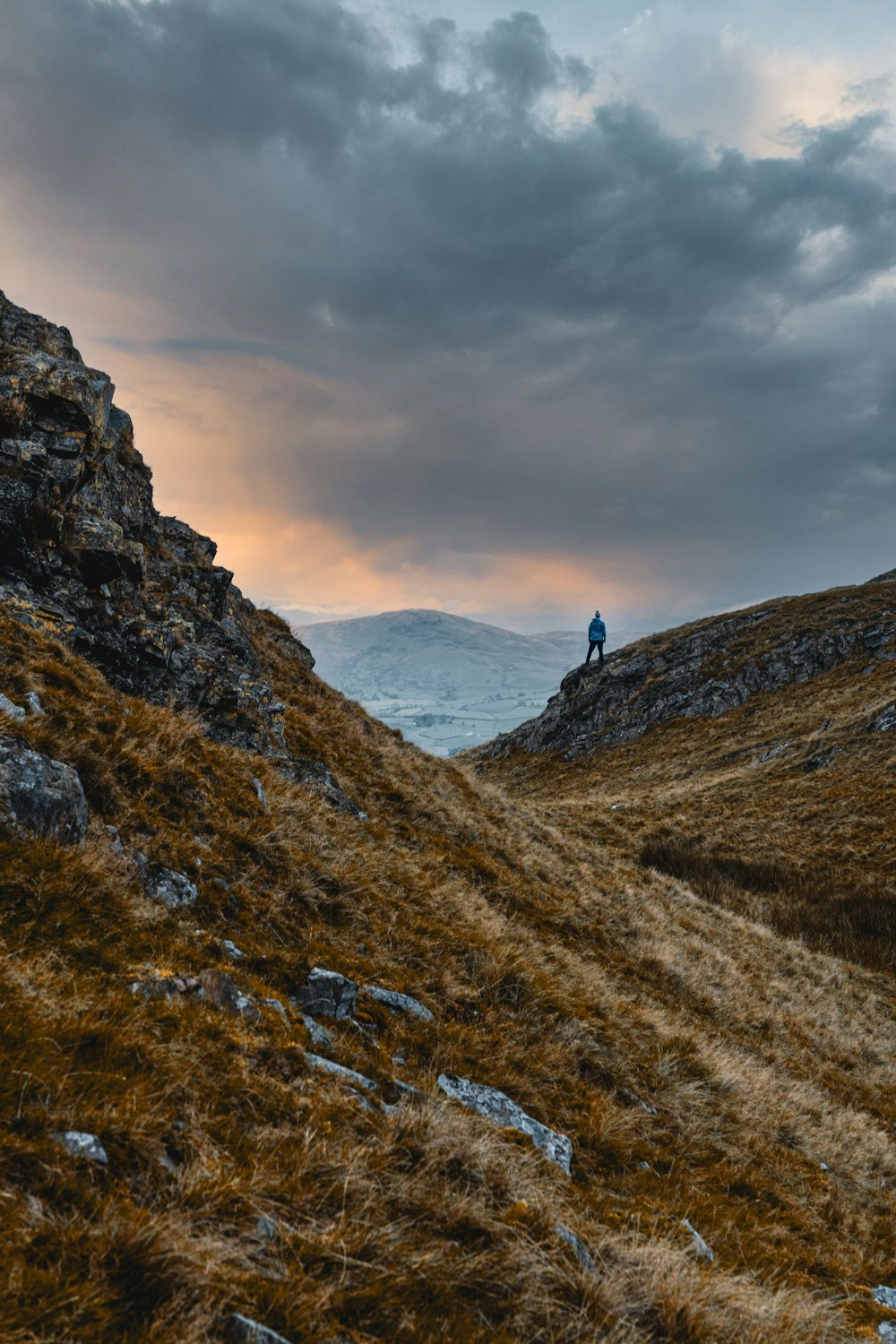 pessoa em pé na montanha rochosa sob o céu nublado durante o dia